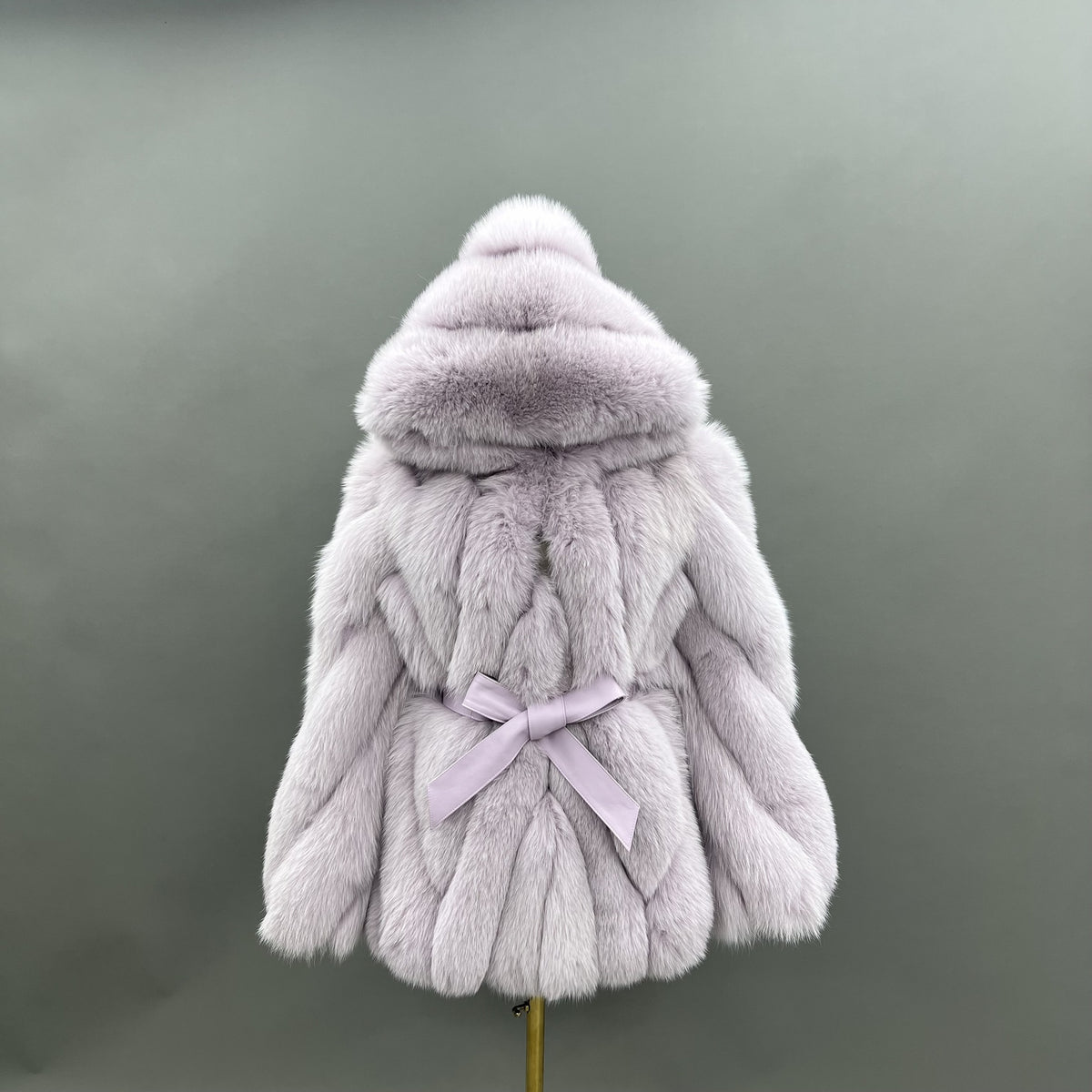 Pale grey fox fur hip-length jacket with an oversized hood, sculpted diagonal panels and tonal waist bow